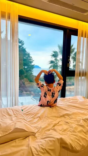 Making a heart with both arms toward the sea from the bed by the window