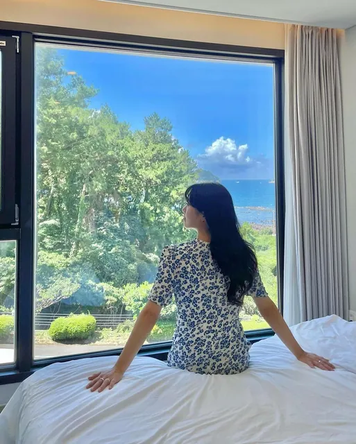 Sitting on the bed facing a window full of green trees and sea