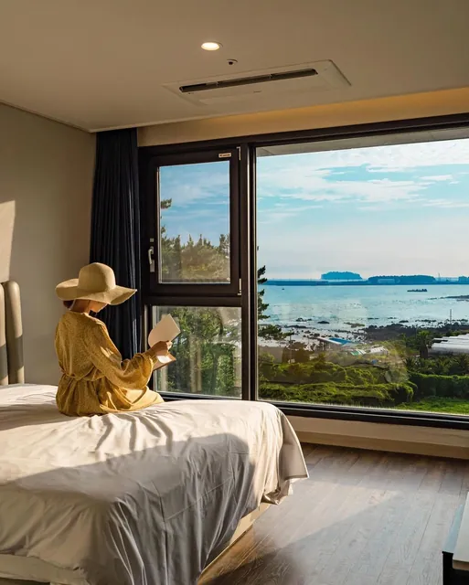 Reading a book on the bed by a sea-view window, in a straw hat